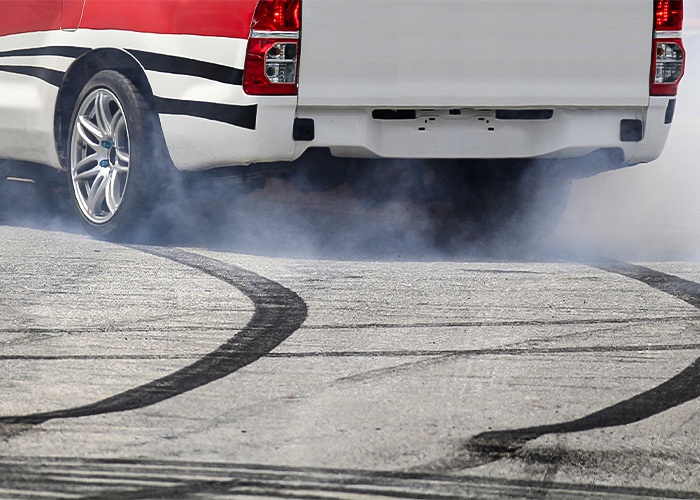 A white vehicle braking, with braking lines visible on the asphalt behind the car. 